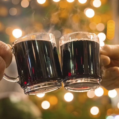 Zwei Hände halten Glühweintassen auf einem Weihnachtsmarkt.